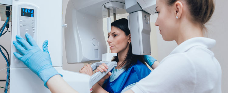 Patient taking a 3d image xray with the help of a dental assistant, their mouth is placed on a the machine ledge while standing